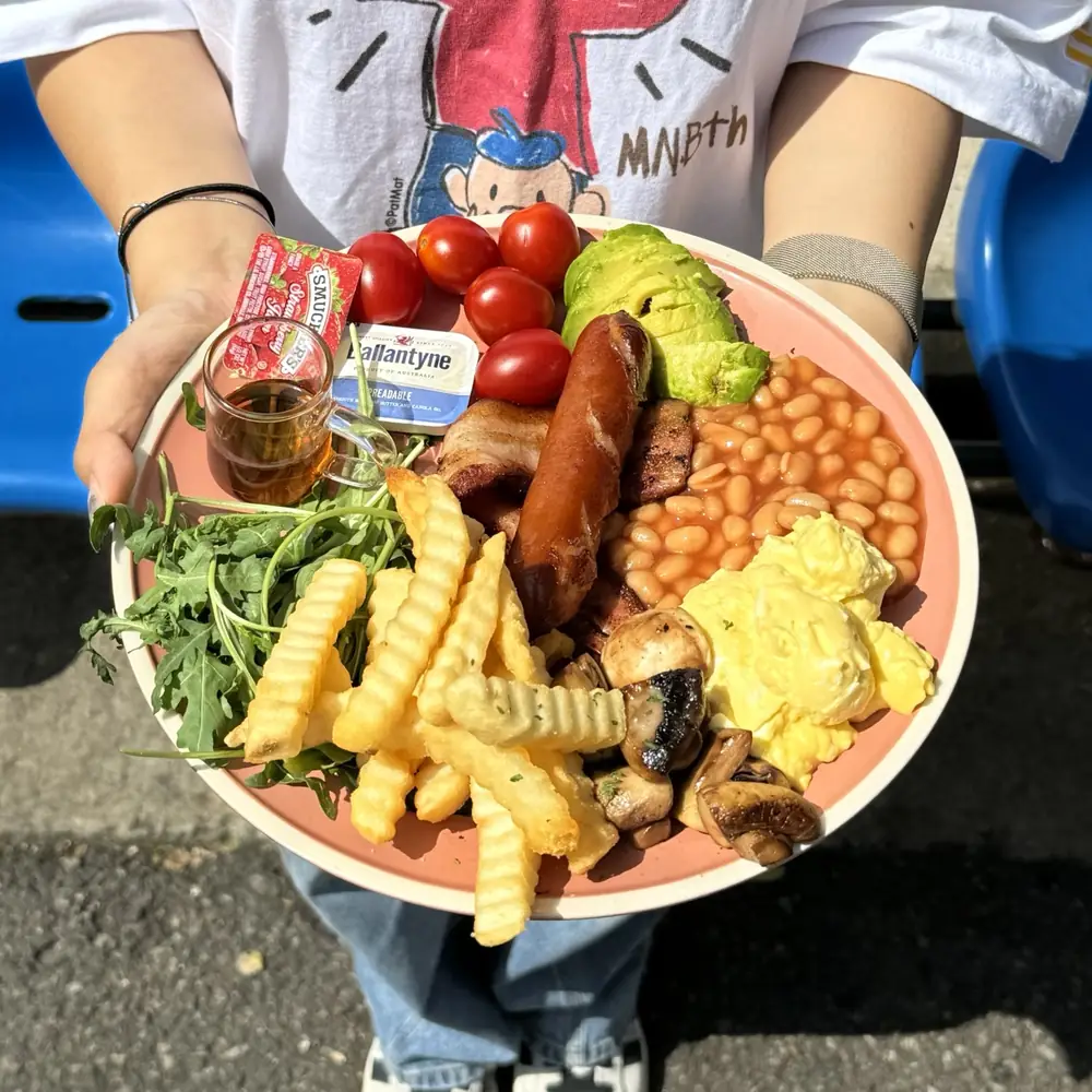 Hands holding a brunch plate of sausage, baked beans, scrambled egg and crinkle-cut fries